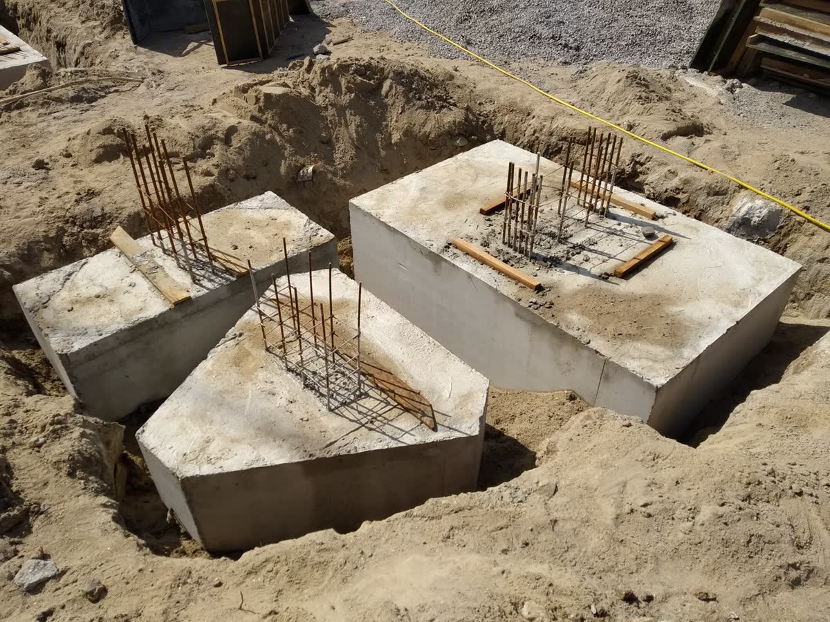 Blocos de fundação concretados na vala, com a ferragem de arranque dos pilares saindo do concreto